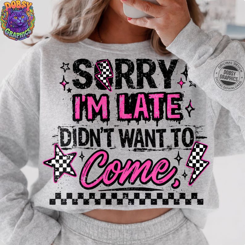 May include: A light gray sweatshirt with the text "SORRY I'M LATE DIDN'T WANT TO COME" in black and pink. The design includes stars, lightning bolts, and a checkered pattern. The sweatshirt has long sleeves.