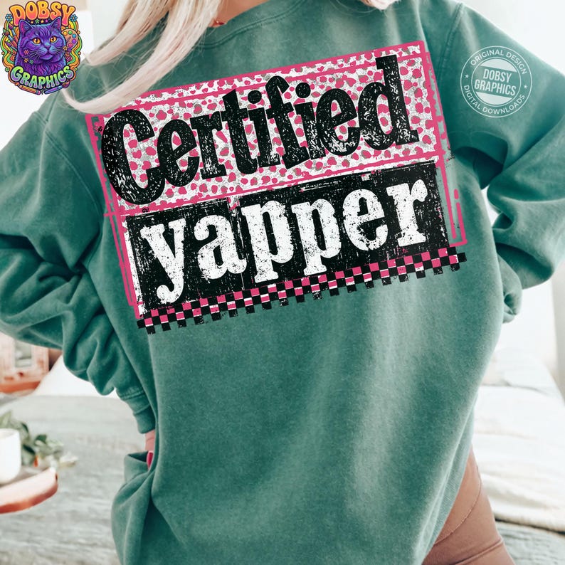 May include: A teal sweatshirt with the words "Certified Yapper" in a black and white design. The text is set against a pink and white polka dot background, with a pink border and a checkered pattern at the bottom.