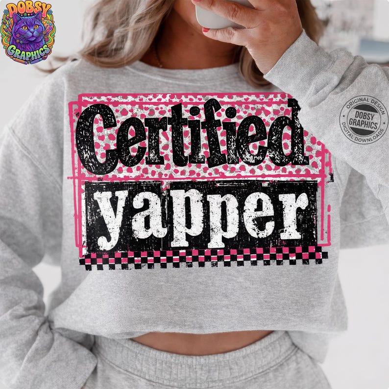 May include: A gray sweatshirt with the text "Certified Yapper" in black and white, with pink accents. The design includes a pink leopard print background and a checkered border. The sweatshirt also features a graphic of a cat.