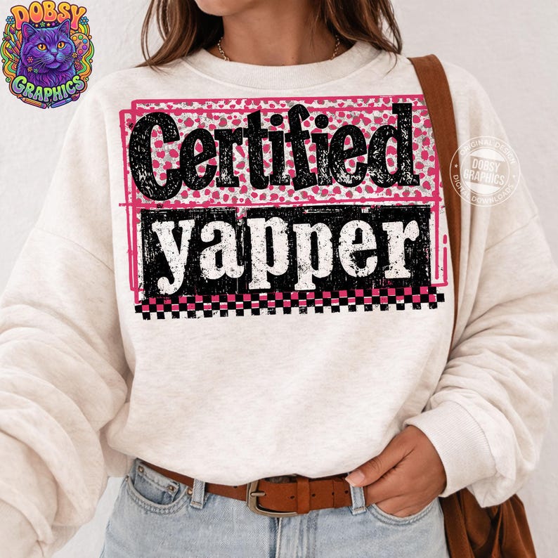 May include: Cream-colored sweatshirt with the text "Certified Yapper" in a black, distressed font, framed by pink and black accents. The design includes a pink dotted pattern and a checkered border. A casual, comfortable top.