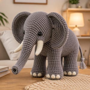 May include: A gray crocheted elephant with large ears, white tusks, and small white toenails. The handmade elephant is sitting on a wooden table. The elephant has a long trunk and a small tail with a tassel.