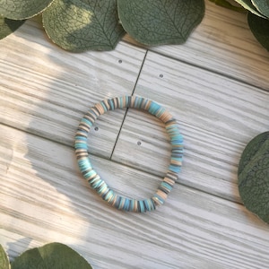 May include: A white ceramic mug with a black handle and the text "But First, Coffee" in a bold, black font. The mug is set against a blurred background, suggesting a cozy setting.