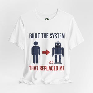 May include: White t-shirt with a graphic design. The design features a stick figure transforming into a robot with the text "BUILT THE SYSTEM THAT REPLACED ME". The text and figures are in navy blue and red.