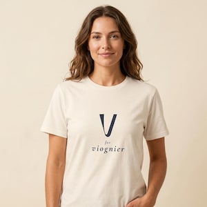 Puede incluir: Una camiseta de manga corta de color crema con una letra V grande de color azul marino oscuro centrada en el pecho. Debajo de la letra, la palabra "for" está impresa en una fuente más pequeña, seguida de la palabra "viognier" en serif.