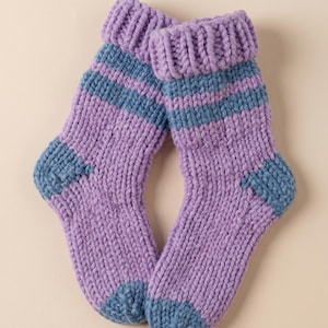 Peut inclure: Une paire de chaussettes tricotées à la main, de couleur lavande avec des détails bleus. Les chaussettes ont une manchette côtelée, un talon et un bout bleus, et des rayures bleues autour de la cheville. Tricot épais.