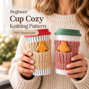 May include: Two reusable cups with knitted cozies, one beige and one dusty pink, each featuring a small pocket holding a gingerbread man cookie. The cups have red and green lids, respectively. Text reads: Beginner Cup Cozy Knitting Pattern PDF Download.