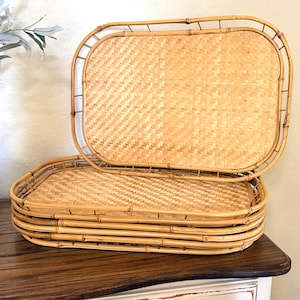 May include: A stack of five rectangular trays crafted from light tan woven bamboo and rattan. Each tray features a sturdy, rounded bamboo frame with a woven base, showcasing a natural light wood finish and a consistent, repeating pattern.