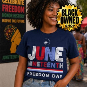 May include: A navy blue t-shirt featuring the text JUNE NINETEENTH FREEDOM DAY in white, red, and light blue striped lettering. Above the text is a white star icon. The design includes a horizontal striped line in red, white, and blue.