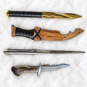 May include: Four decorative knives arranged vertically. The top knife has a black twisted handle and gold blade. The second is a tan bone-like knife with a black wrapped grip. The third is a silver metal letter opener. The bottom is a serrated knife with a textured antler handle.