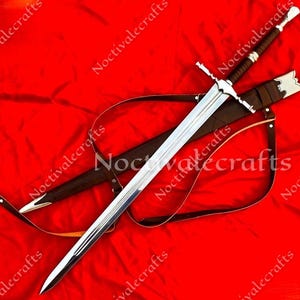 May include: A long, silver sword with a cross-shaped hilt and a brown leather-wrapped handle. The sword rests in a brown leather sheath with a silver accent, and a leather strap. The background is a solid red.