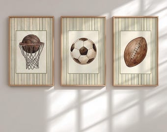 May include: Set of three framed watercolor prints featuring sports balls. Includes a basketball in a hoop, a soccer ball, and a football. Each print has a cream-colored background with a green striped border and a wooden frame.