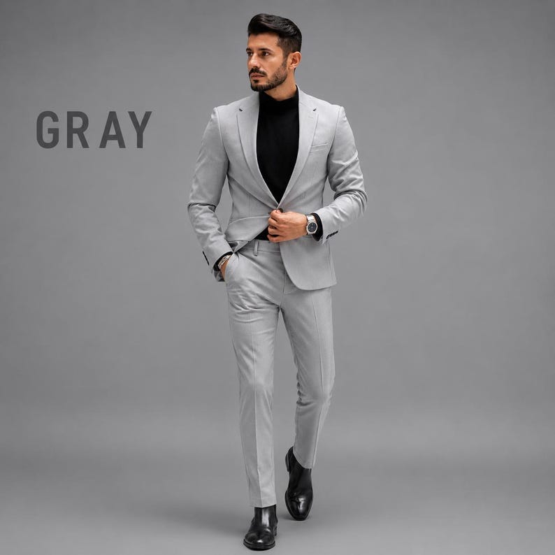 May include: A light gray suit consisting of a single-breasted blazer with notched lapels and matching slim-fit trousers. The suit is worn over a black mock-neck shirt. The word GRAY is printed in dark letters on the left side of the image.