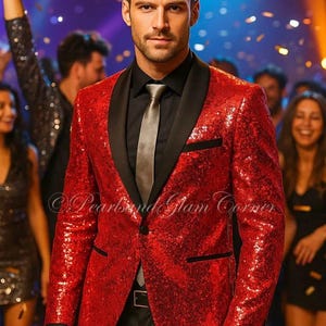 Op de afbeelding: Een rode blazer met pailletten en zwarte revers, gedragen met een zwart overhemd, grijze stropdas en zwarte broek. De afbeelding toont een man in een feestelijke setting met confetti en een vage achtergrond. De tekst "Pearls and Glam Corner" is zichtbaar.