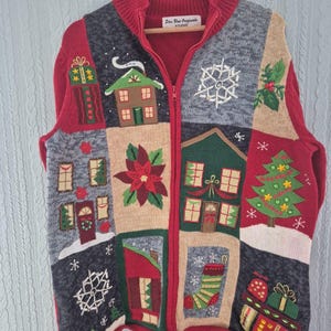 Könnte beinhalten: Ein rot, grau und beige gestrickter Reißverschluss-Pullover mit einem Patchwork-Design aus Weihnachtsmotiven wie Häusern, einem Weihnachtsbaum, einem Strumpf, Schneeflocken, Weihnachtssternen und Geschenken. Das Etikett zeigt Star Blue Originals Studio.
