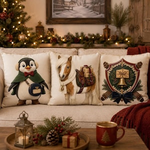 Three decorative Christmas pillows sit on a sofa, featuring illustrations of a penguin, a pony, and a gift crest.