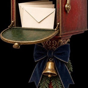 A red postbox with gold trim and a green interior, containing envelopes and decorated with a blue velvet bow.