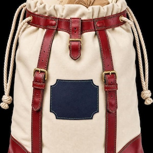 A canvas drawstring bag with red leather straps, brass buckles, and envelopes sticking out of the top.
