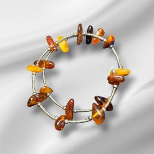 May include: A silver bracelet with multiple amber-colored stones. The stones vary in shape and hue, ranging from light yellow to dark brown. The bracelet is made of two silver bands connected by smaller silver pieces.