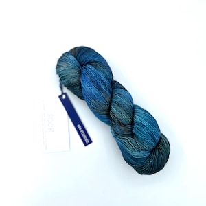 May include: A skein of blue and teal hand-dyed yarn, with a tag reading "404 Fluidic". The yarn is tightly twisted, displaying colour and texture variations. The background is plain white.