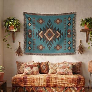 Puede incluir: Un tapiz con estampado geométrico turquesa y marrón cuelga sobre un diván con cojines estampados. El diván tiene un diseño tie-dye naranja y marrón. Las plantas en macetas y una lámpara tejida completan la habitación de estilo bohemio.