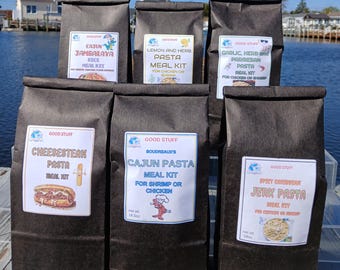 Könnte beinhalten: Sechs dunkelbraune Papiertüten, die jeweils mit einem anderen Pasta-Fertiggericht gekennzeichnet sind. Die Kits umfassen Cajun Jambalaya, Zitronen- und Kräuter-Pasta, Knoblauch-Kräuter- und Parmesan-Pasta, Cheesesteak-Pasta, Cajun-Pasta und Spicy Caribbean Jerk Pasta.