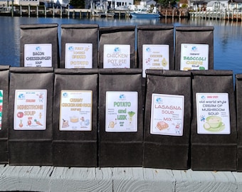 Könnte beinhalten: Eine Reihe von dunkelbraunen Papiertüten mit verschiedenen Suppenmischungen. Jede Tüte hat ein Etikett mit dem Namen der Suppe und einer Grafik. Suppensorten sind unter anderem Bacon Cheeseburger, Chicken Pot Pie und Taco Soup.