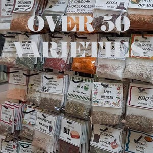 May include: A display of various dip mixes in clear plastic bags, each labeled with flavor names like "Chili Cheese and Bacon" and "Sweet Tomato Salsa." The text "OVER 50 VARIETIES" is prominently displayed.