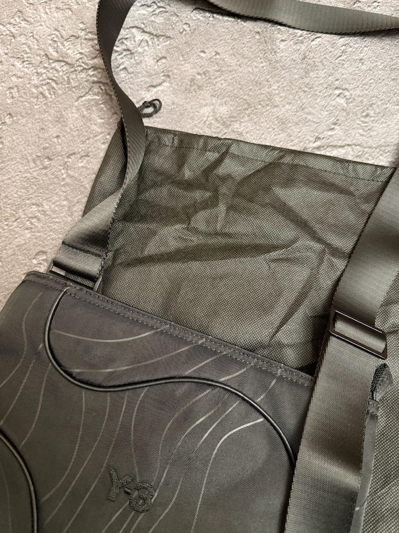 Peut inclure: Sac messager gris fonc&eacute; avec un motif de vagues et une bandouli&egrave;re. Le sac a une fermeture &agrave; rabat et un petit logo sur le devant. Le sac est fait d'un mat&eacute;riau durable et a un design simple et moderne.