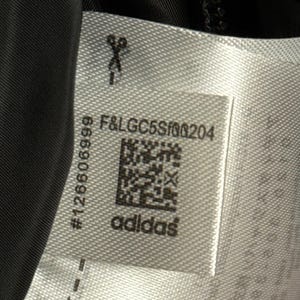 Peut inclure: Gros plan sur une &eacute;tiquette blanche avec le logo Adidas et le texte "F&LGC5Sf00204". L'&eacute;tiquette comprend &eacute;galement un code QR et le num&eacute;ro "126606999". Des ic&ocirc;nes de ciseaux sont imprim&eacute;es sur l'&eacute;tiquette.