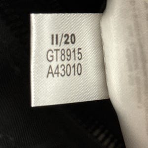 Peut inclure: Gros plan sur une &eacute;tiquette blanche avec du texte noir. L'&eacute;tiquette indique "11/20", "GT8915" et "A43010". L'&eacute;tiquette est attach&eacute;e &agrave; un tissu noir, possiblement un v&ecirc;tement.