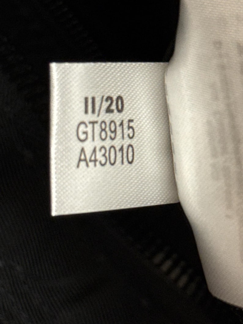 Peut inclure: Gros plan sur une &eacute;tiquette blanche avec du texte noir. L'&eacute;tiquette indique "11/20", "GT8915" et "A43010". L'&eacute;tiquette est attach&eacute;e &agrave; un tissu noir, possiblement un v&ecirc;tement.