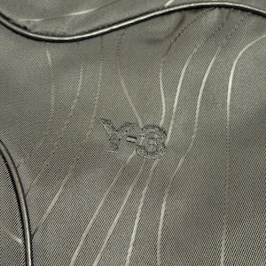 Peut inclure: Gros plan sur un tissu vert fonc&eacute; avec un motif &agrave; rayures verticales. Le logo Y-3 est brod&eacute; en bas au centre. Une bordure noire et arrondie est visible en haut et &agrave; gauche de l'image.