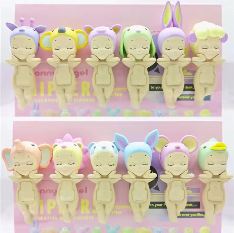 May include: A collection of small, whimsical figurines, each dressed in a different animal-themed hat. The figurines are in various pastel colors, including pink, yellow, and blue. The text "Sunny Angel" is visible on the packaging.