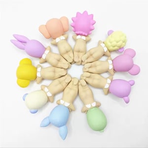 May include: A collection of colorful, whimsical bottle stoppers. Each stopper features a hand-shaped base with a decorative top in various shapes and colors, including a bunny, elephant, and flower. The stoppers are arranged in a circular pattern.