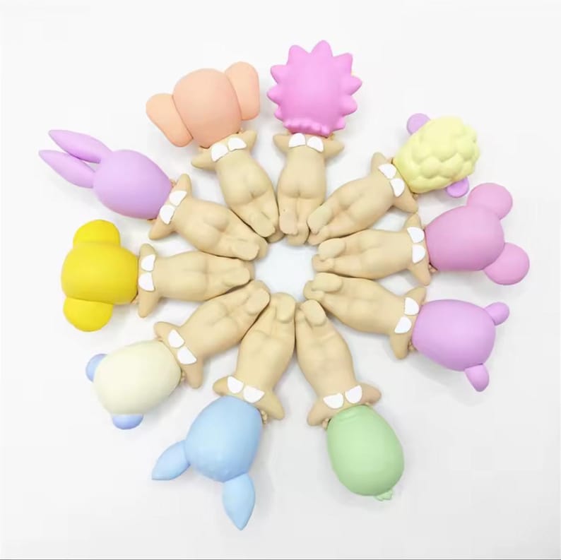 May include: A collection of colorful, whimsical bottle stoppers. Each stopper features a hand-shaped base with a decorative top in various shapes and colors, including a bunny, elephant, and flower. The stoppers are arranged in a circular pattern.