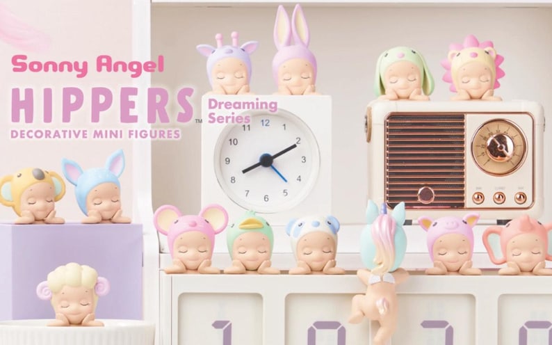 May include: A collection of Sonny Angel Hippers decorative mini figures from the Dreaming Series. The figures are in various animal and fantasy-themed costumes, including a giraffe, bunny, and lion. The figures are displayed on a white shelf with a clock and a vintage radio.