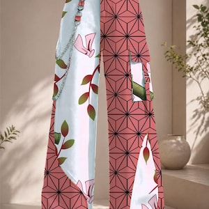 May include: High-waisted wide-leg pants featuring a split design. One side displays a pink and black geometric star pattern, while the other is white with green leaf and pink floral motifs. The pants include a silver chain detail and cargo pockets.