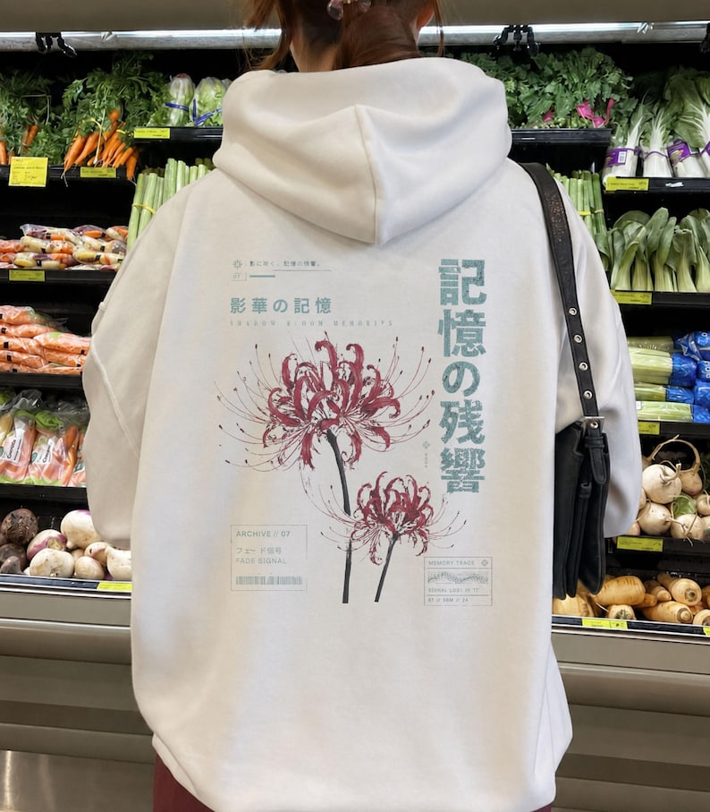 May include: A white hooded sweatshirt featuring a graphic print on the back. The design includes two red spider lily flowers, Japanese text, and English phrases like Shadow Bloom Memories, Archive 07, and Fade Signal in a minimalist layout.