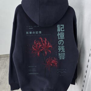 May include: A dark charcoal gray hooded sweatshirt featuring a back graphic of two red spider lilies. The design includes Japanese text, the phrase "Archive 07," "Fade Signal," and "Memory Trace" printed in white and light blue lettering.