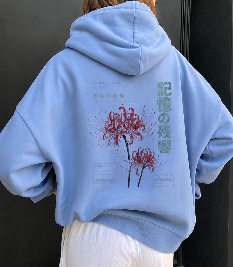 May include: A light blue hooded sweatshirt featuring a graphic on the back with two red spider lily flowers. The design includes Japanese text, specifically 記憶の残響 and 影の記憶, along with small rectangular boxes containing additional text.