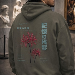May include: An olive green hooded sweatshirt featuring a graphic on the back with two red spider lily flowers, light blue Japanese text, and smaller white text including the words Archive 07 and Fage Signal printed in a clean layout.
