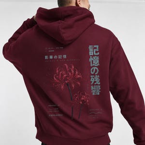 May include: A deep burgundy hooded sweatshirt featuring a graphic on the back with two red spider lily flowers. The design includes Japanese text, the English words "ARCHIVE 07" and "FADE SIGNAL," and additional small text elements in a muted grey.
