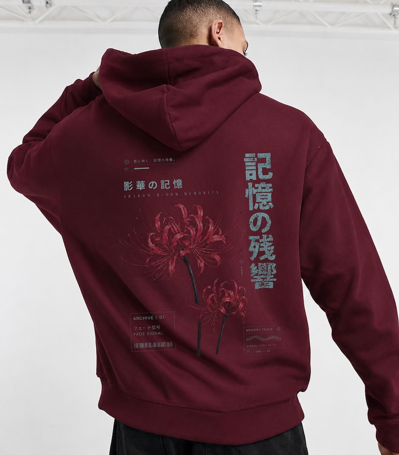 May include: A deep burgundy hooded sweatshirt featuring a graphic on the back with two red spider lily flowers. The design includes Japanese text, the English words "ARCHIVE 07" and "FADE SIGNAL," and additional small text elements in a muted grey.
