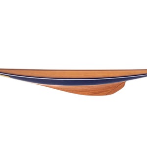 Könnte beinhalten: Ein Holzmodell-Segelboot mit schlankem Design. Der Rumpf ist hellbraun, mit einem dunkelblauen Streifen und einem dünnen weißen Streifen. Das Boot ist etwa 61 cm lang.