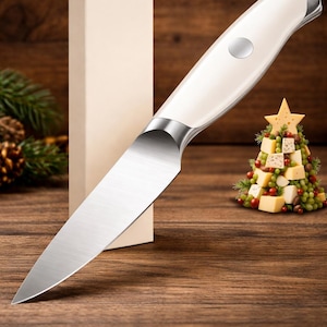 Peut inclure: Un couteau &agrave; fromage avec un manche cr&egrave;me et une lame argent&eacute;e. Le couteau est pr&eacute;sent&eacute; sur une surface en bois &agrave; c&ocirc;t&eacute; d'une bo&icirc;te cadeau et d'un sapin de No&euml;l en fromage d&eacute;coratif. Le couteau est con&ccedil;u pour couper le fromage.