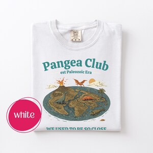 Peut inclure: T-shirt blanc avec un motif graphique. Le motif pr&eacute;sente les mots "Pangea Club" et "est Paleozoic Era", une carte de la Terre avec des dinosaures, un volcan et le texte "WE USED TO BE SO CLOSE."