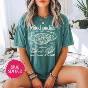 May include: Teal-colored t-shirt with the word "Mitochondria" and a diagram of a cell's powerhouse. The shirt also features the text "Powerhouse of The Cell!" and "we make ATP so you don't have to."