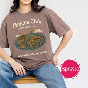 Peut inclure: T-shirt marron avec un motif du Pangea Club, une carte pr&eacute;historique et le texte "WE USED TO BE SO CLOSE." Le motif comprend des dinosaures, un volcan et un soleil. Le t-shirt est de coupe d&eacute;contract&eacute;e.