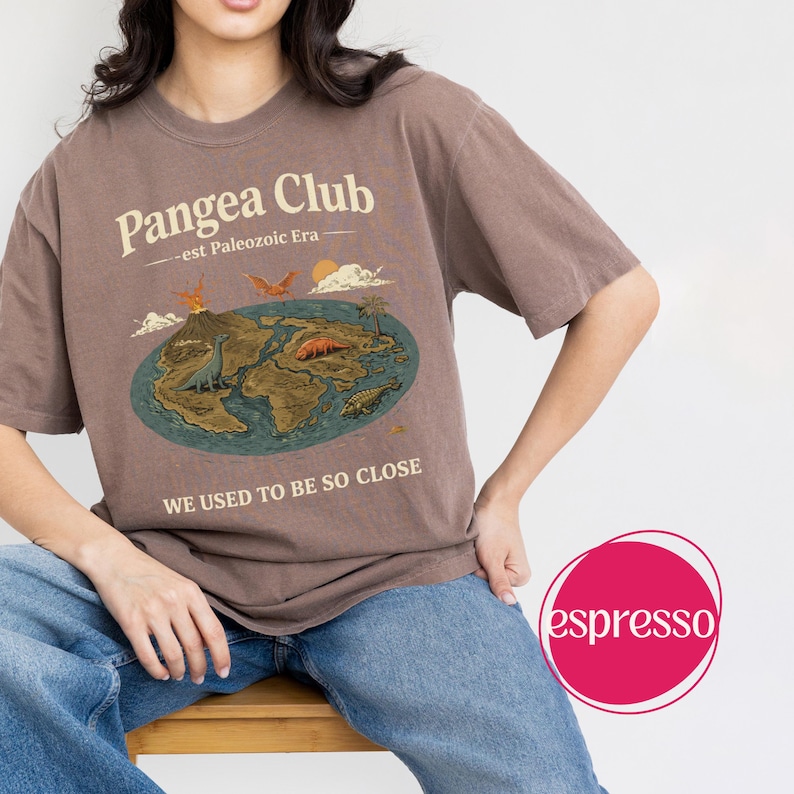 Peut inclure: T-shirt marron avec un motif du Pangea Club, une carte pr&eacute;historique et le texte "WE USED TO BE SO CLOSE." Le motif comprend des dinosaures, un volcan et un soleil. Le t-shirt est de coupe d&eacute;contract&eacute;e.