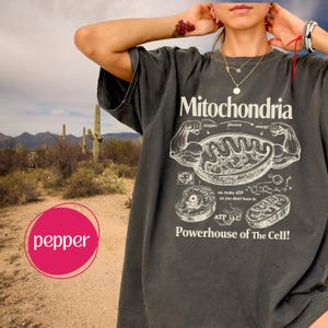 May include: Dark grey t-shirt with the word "Mitochondria" and a diagram of a cell's powerhouse. The shirt also features the text "Powerhouse of The Cell!" and other scientific details. The shirt is a relaxed fit.